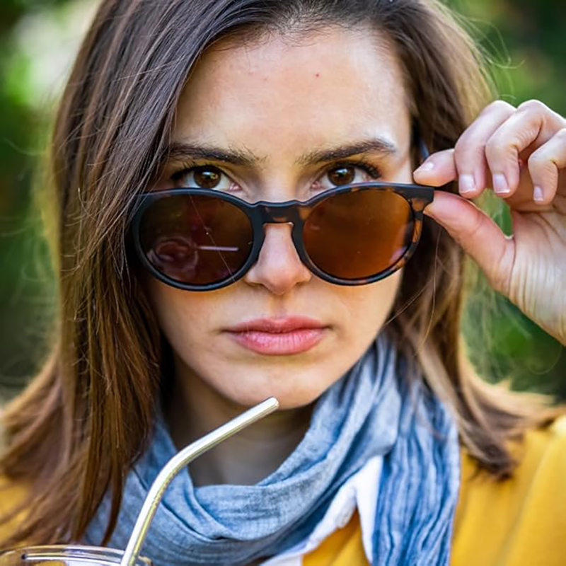 Mujer bonita al aire libre con gafas de sol mirando a la cámara mientras toma una bebida